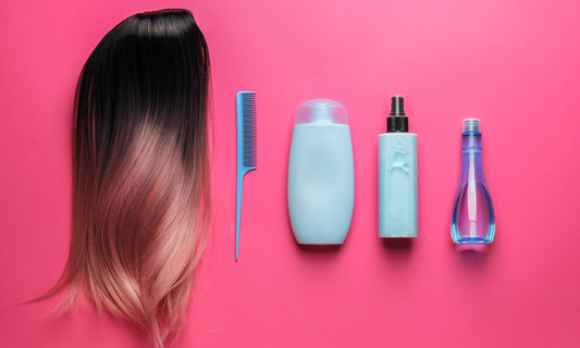 Flat lay of an ombré wig, comb, shampoo, conditioner, and spray bottle for wig care on a pink background